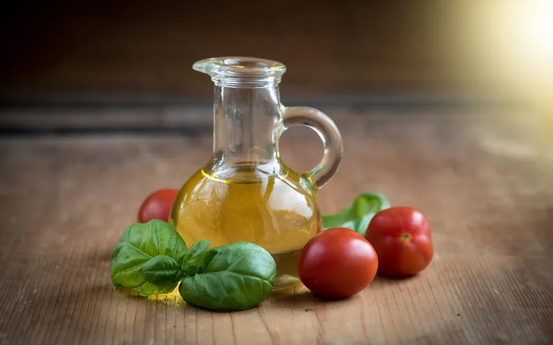 Une carafe d’huile d’olive, des tomates et du basilic sur une table en bois