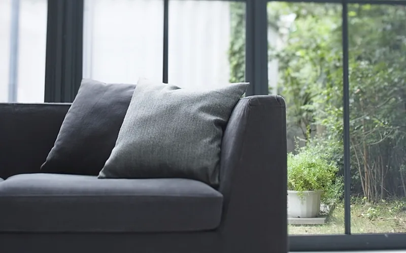 Grande baie vitrée ouverte sur le jardin, canapé et coussins gris