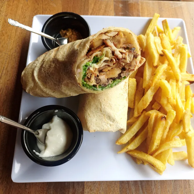 Shawarma roulé coupé en deux, frites et deux sauces sur une assiette blanche